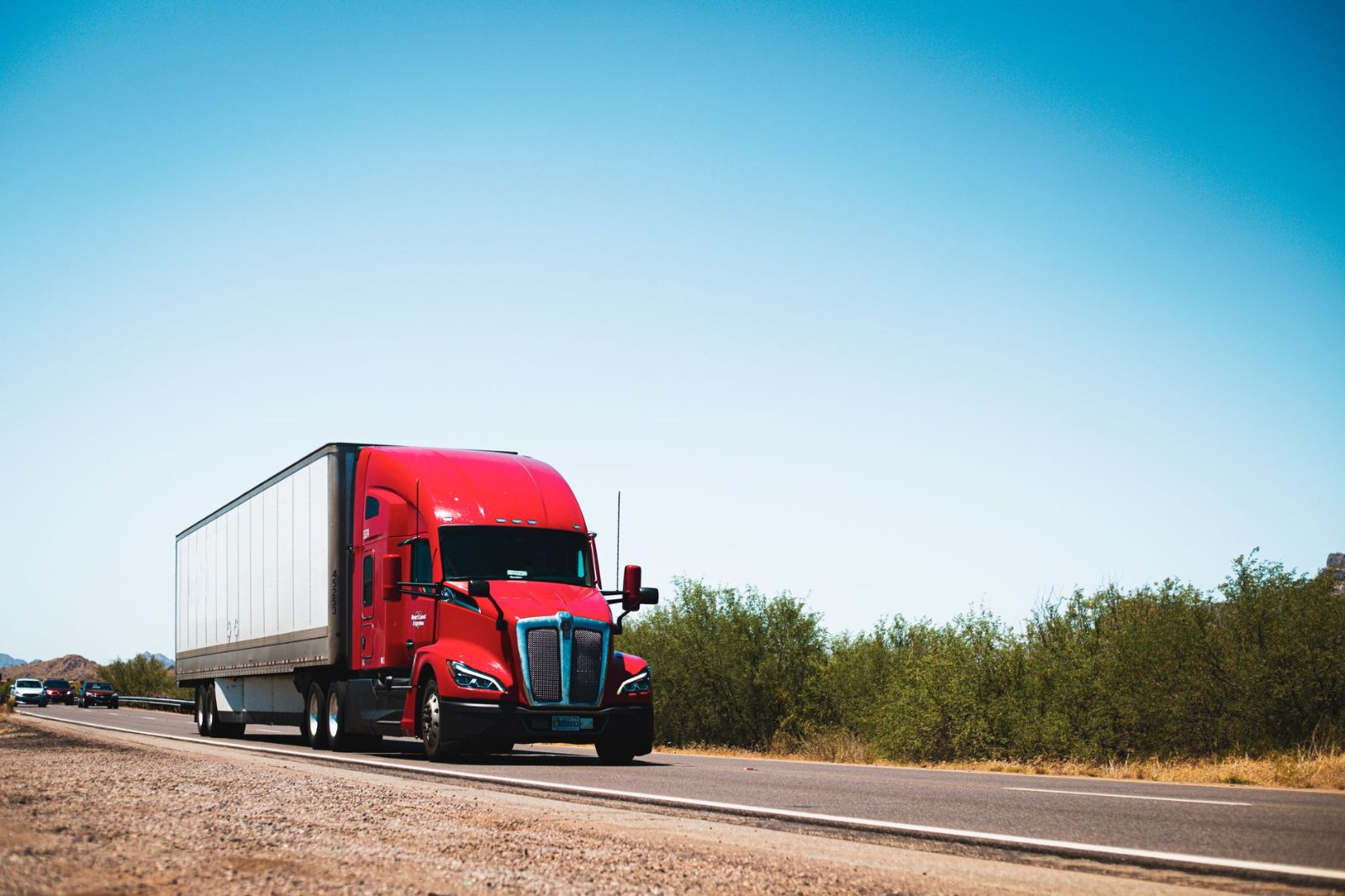 A clean dry-van tractor-trailer running an open interstate lane in flat mid-morning daylight, guardrail and lane markings